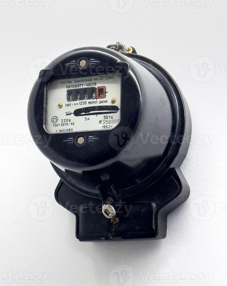 A close up of a vintage Soviet era single phase electric meter mounted on a white wall. The black housing and retro design emphasize its historical value and engineering significance photo