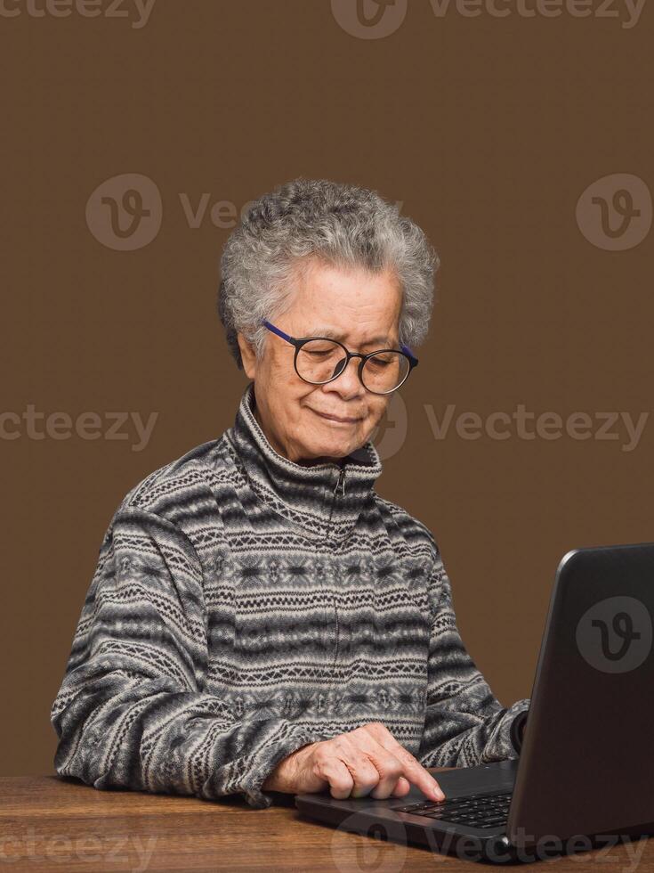 An elderly Asian woman uses a laptop to search for data from the internet while sitting at the table photo