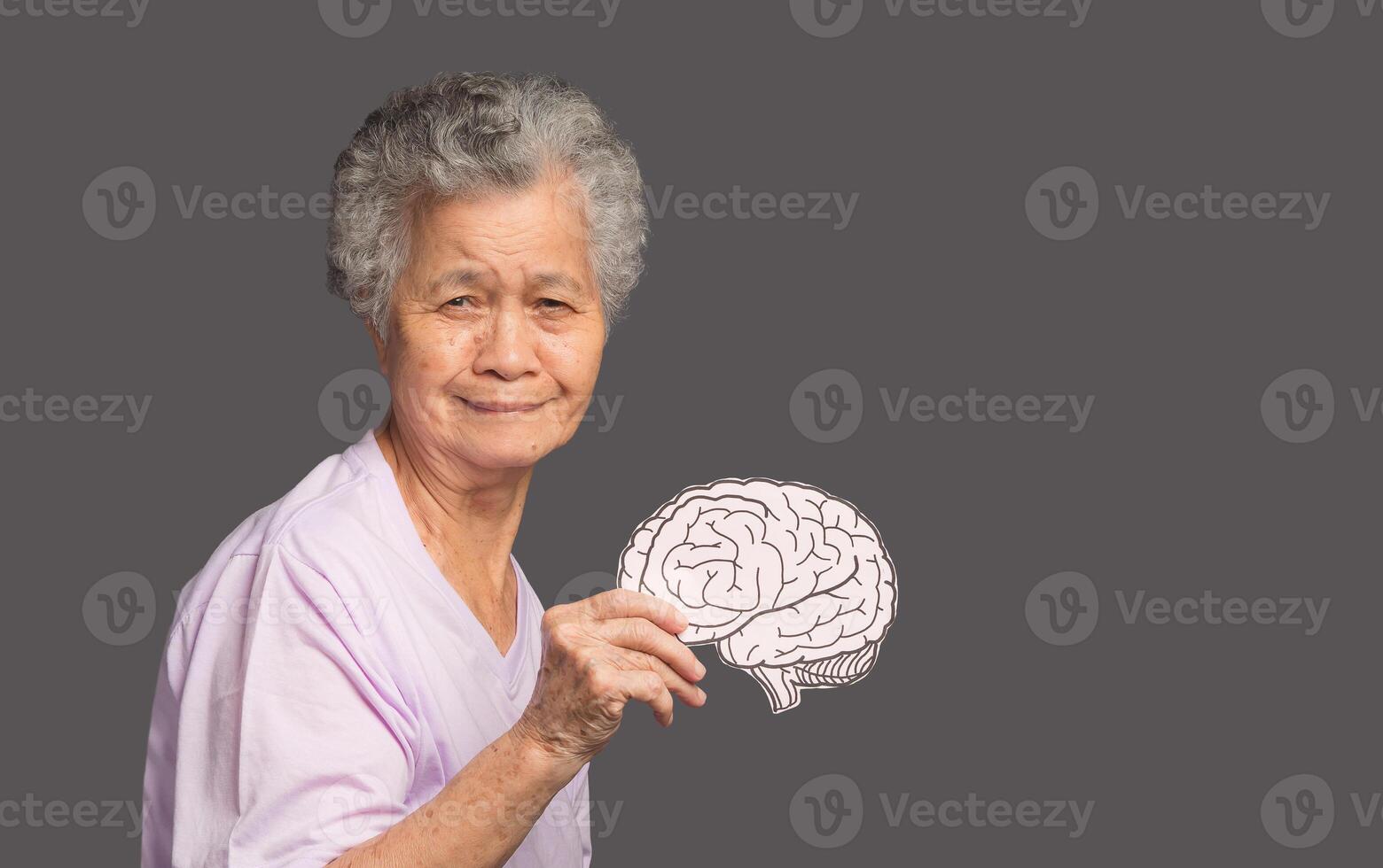 A senior woman holding a brain symbol while standing on a gray background photo