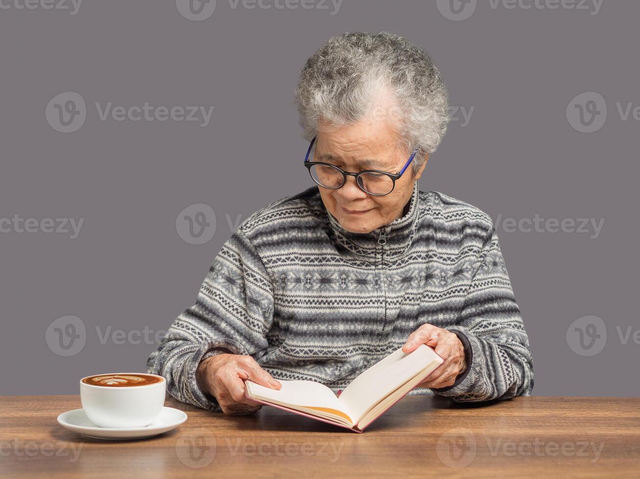 An elderly Asian woman with short white hair read a book with a smile while sitting at home photo
