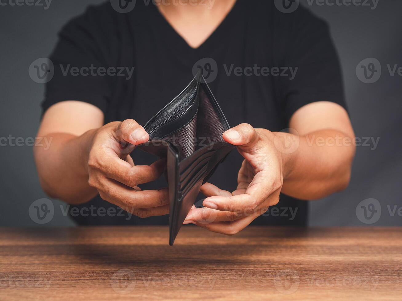 A young man opens an empty wallet while sitting at the table photo