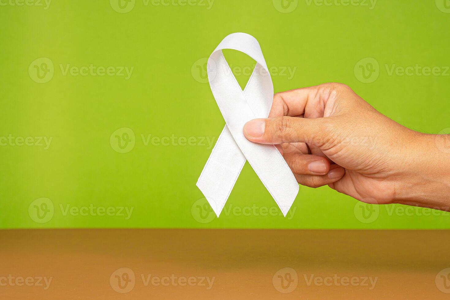 Symbol of the fight against lung cancer. Hand holding a white ribbon with a green background photo