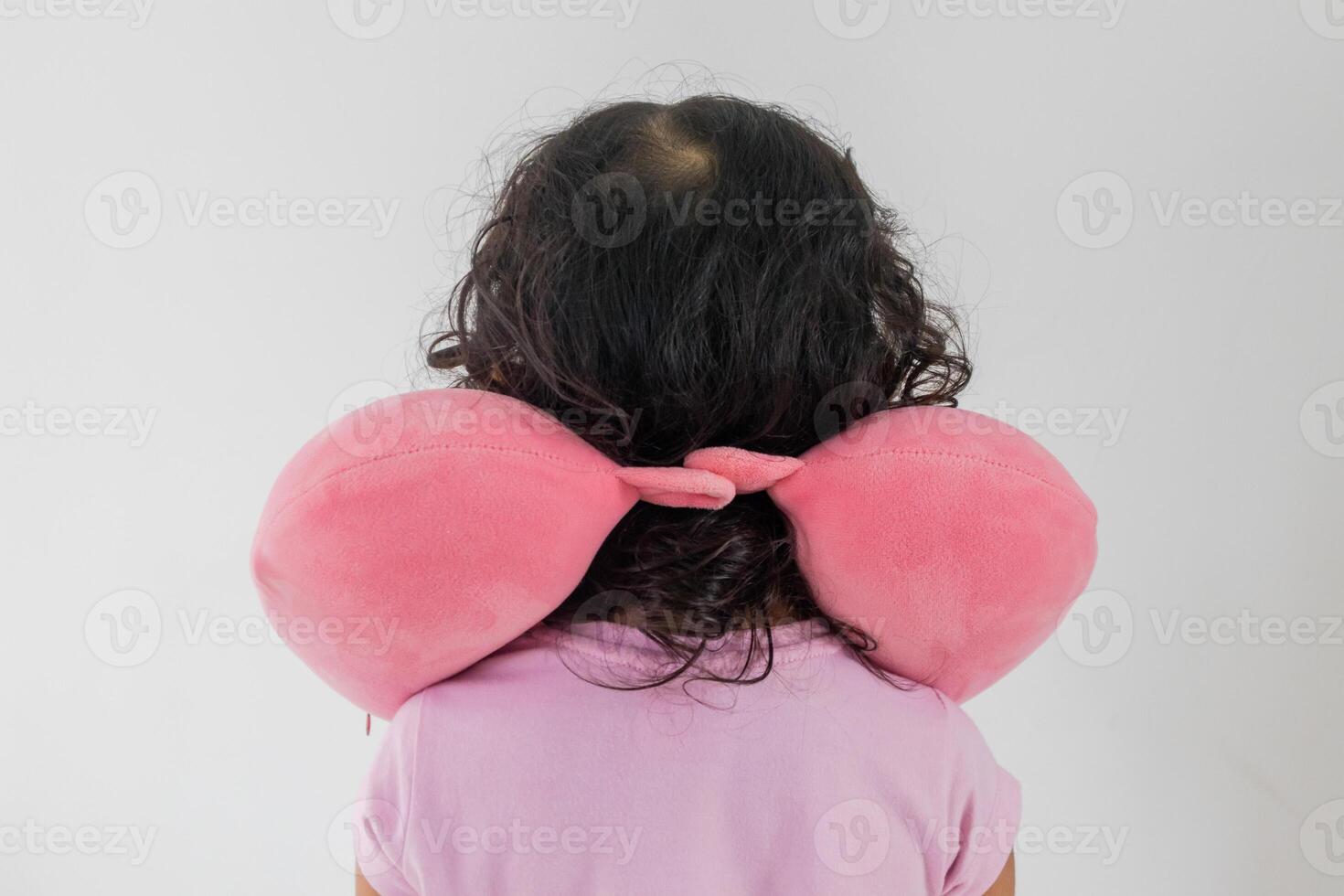 Back view of a little Asian girl wearing a pink travel neck pillow on a white background photo