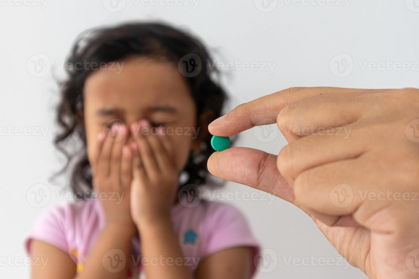 A mother's hand holding a tablet medicine with a little girl covering her mouth with both hands. The concept of children refusing to take medicine. photo