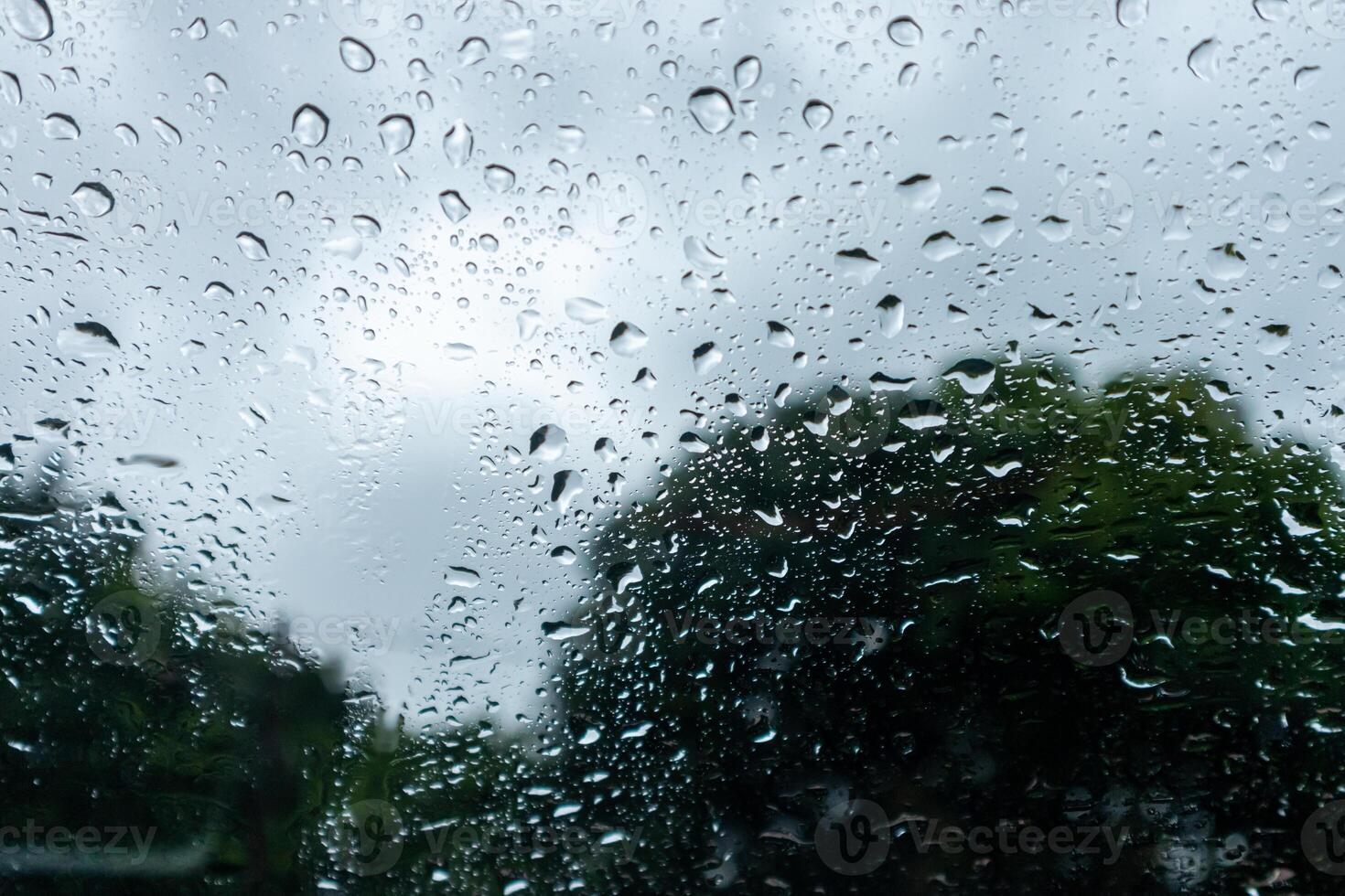 Raindrops on car window with cloudy sky and trees in the background photo