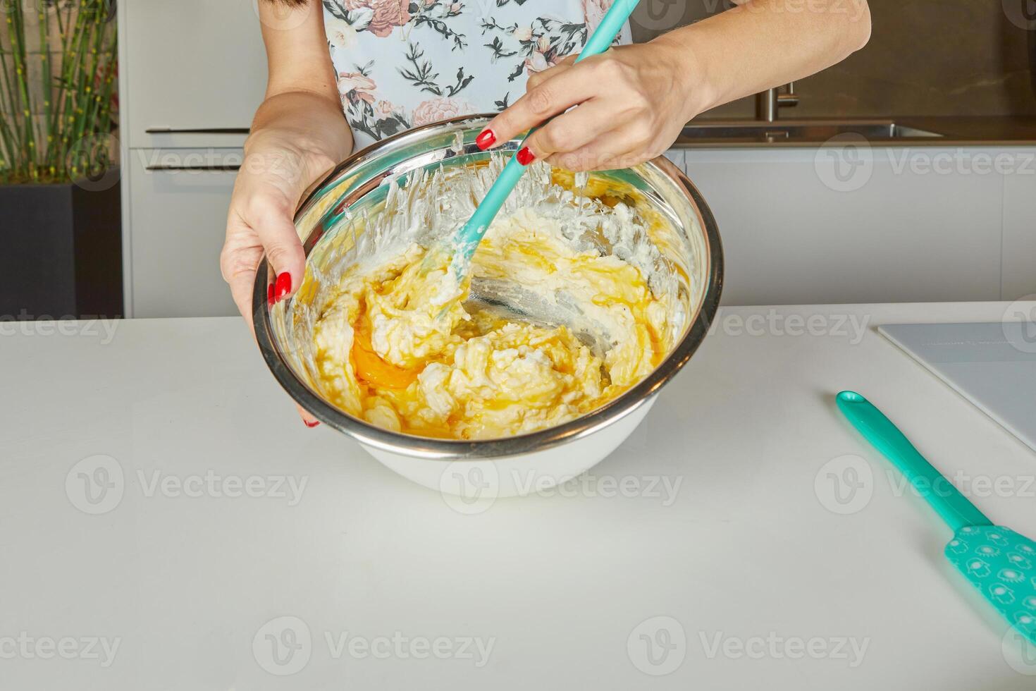 A woman stirs the final batter in a large metal mixing bowl, preparing the ingredients for baking or cooking a homemade dish. photo
