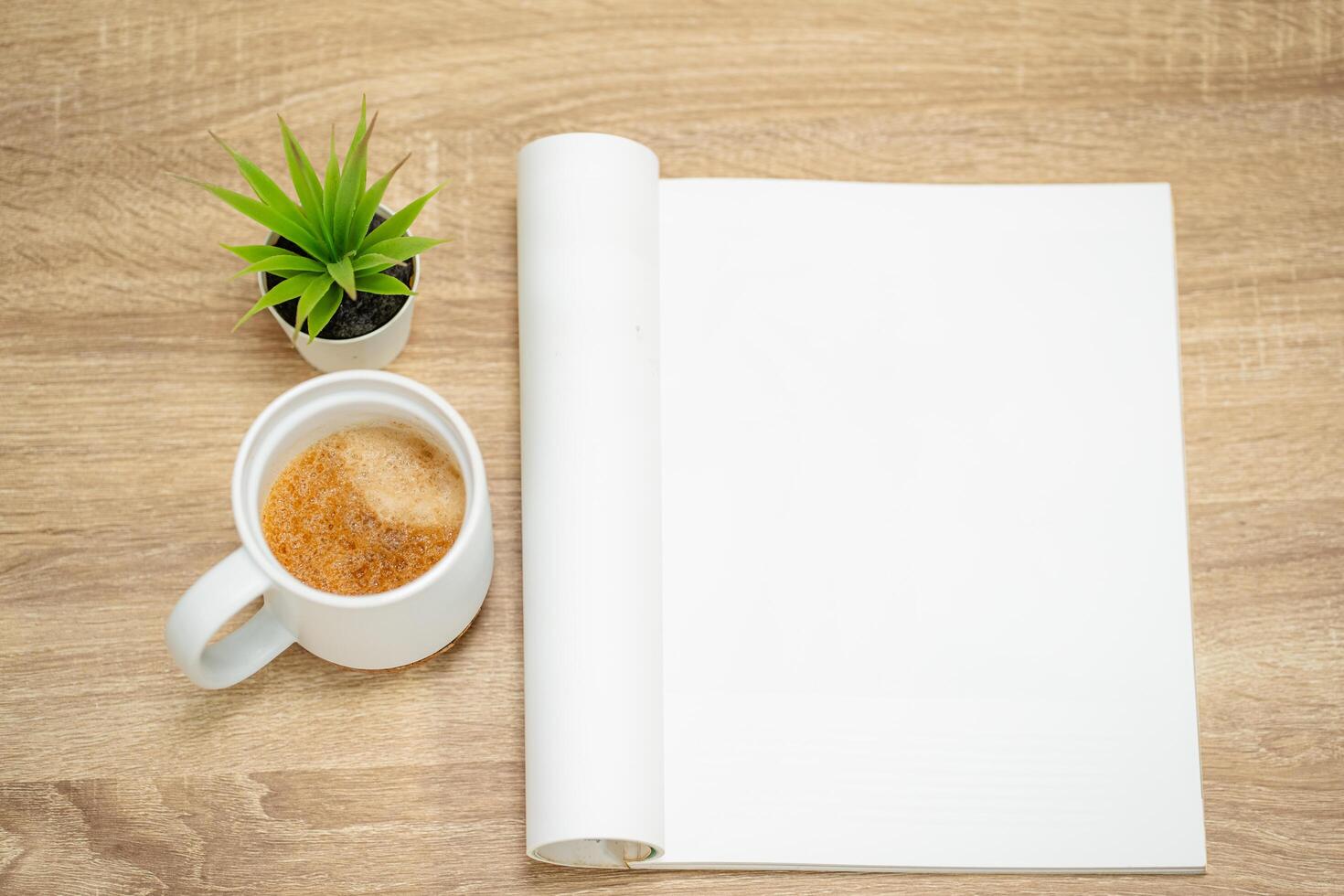 Glass of hot coffee with an open empty magazine on a wooden table or desk from above in mock up concept. photo