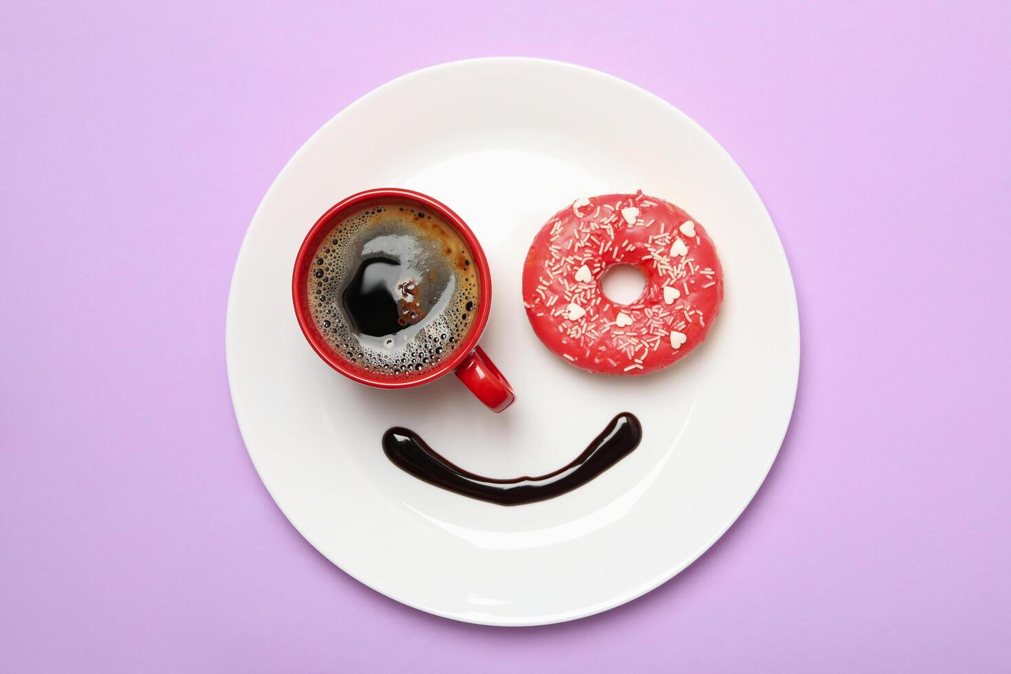 Smile face made of plate with donut, chocolate sauce and coffee on violet background photo