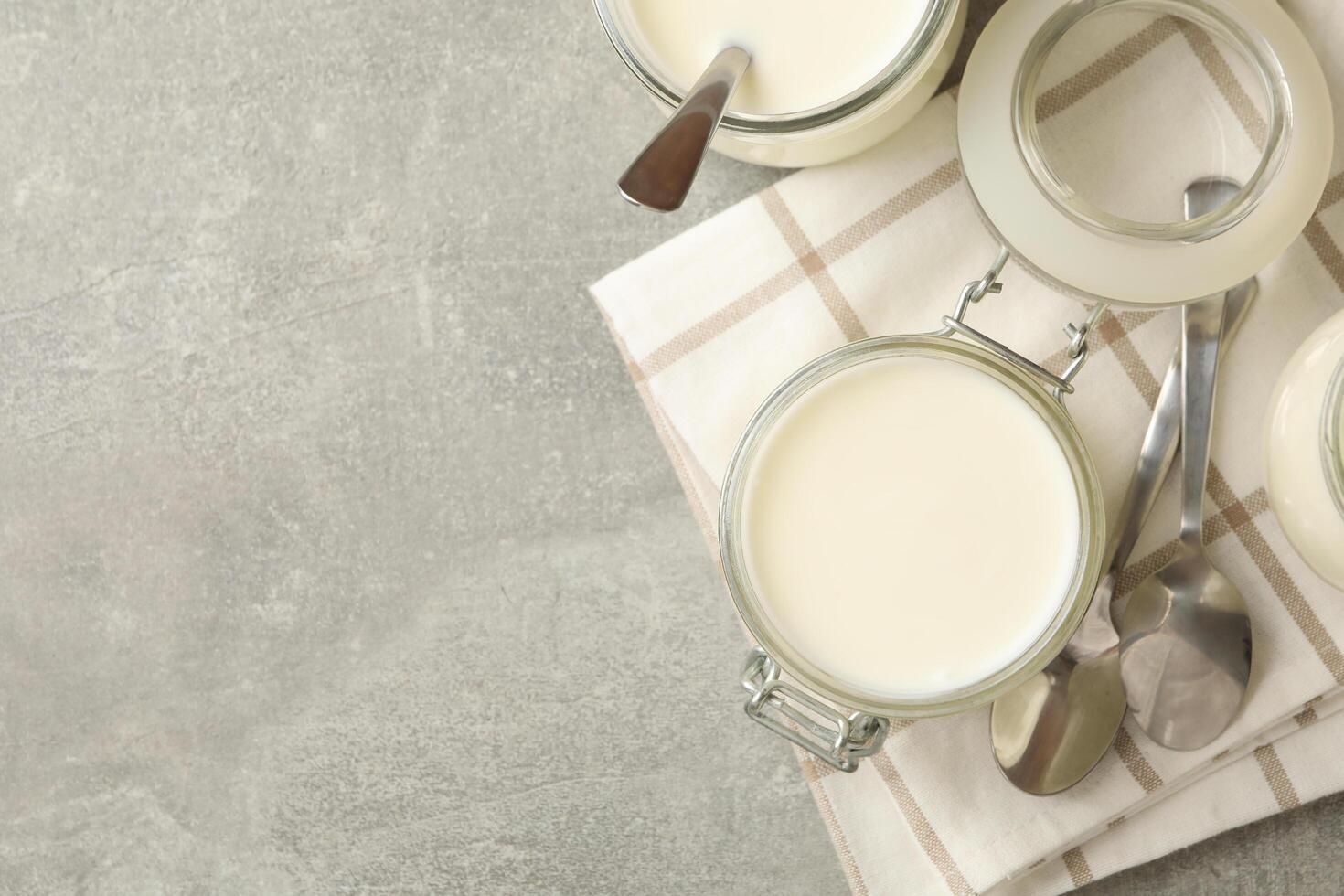 Glass jars of yogurt, spoons and napkin on gray background photo
