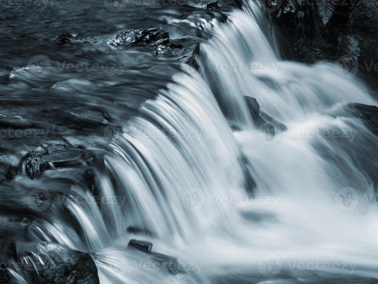 A man is sitting on a rock next to a waterfall photo