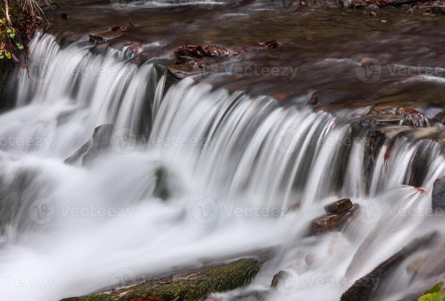 A small waterfall flowing over rocks in a stream photo