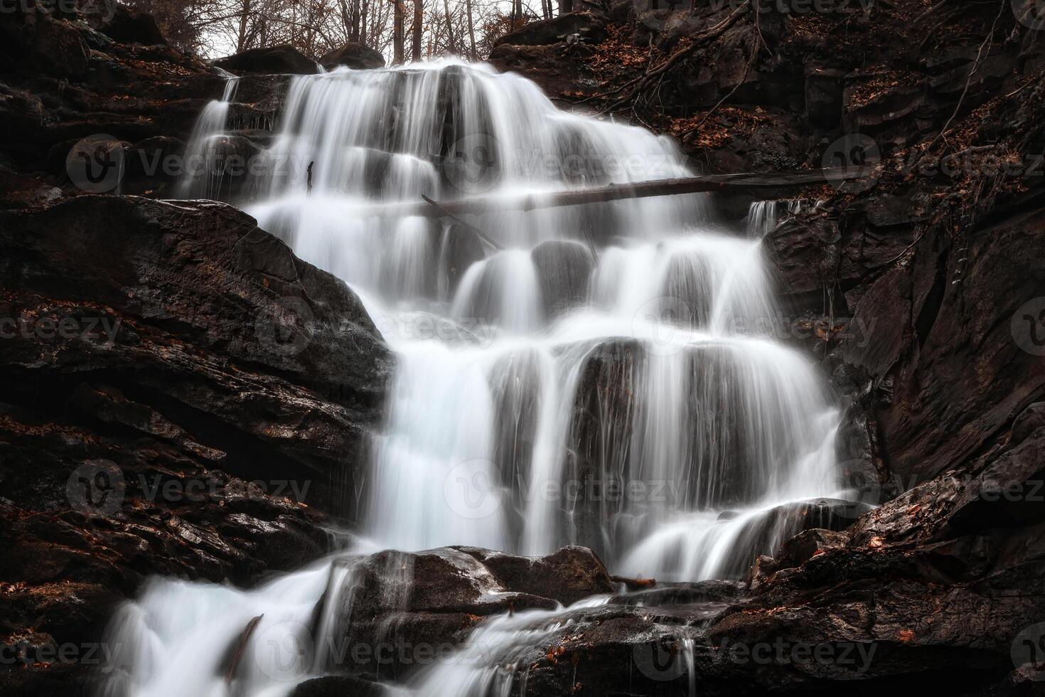 A waterfall in the woods with a large rock photo