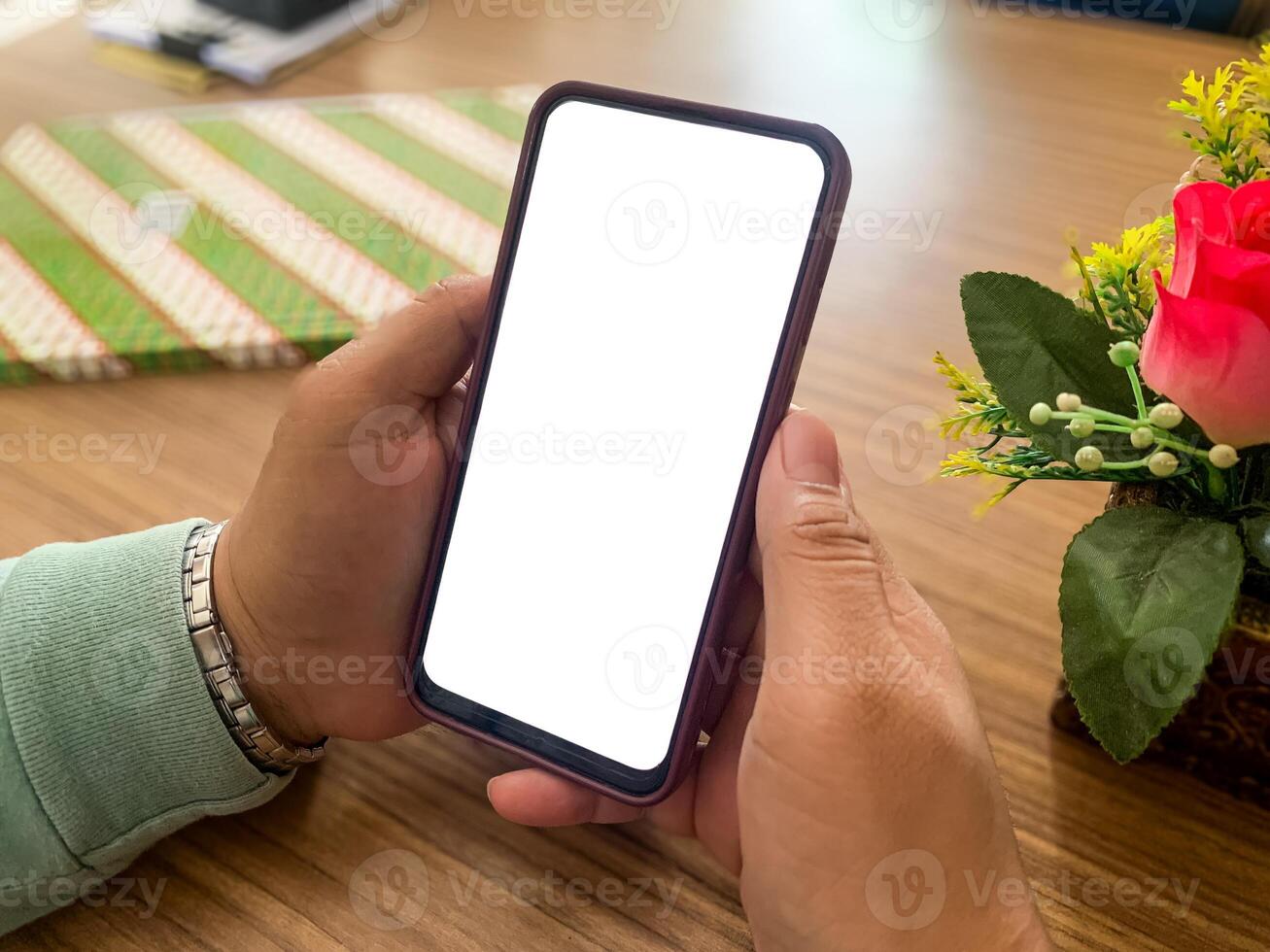 a woman's hand is holding a smartphone or cell phone with a blank white screen on an office desk. mockup of a smartphone with a blank white screen photo