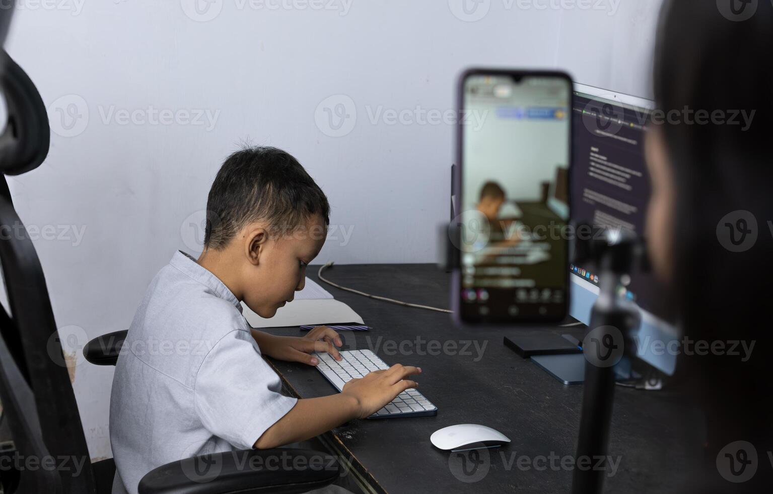 Asian boy is doing his homework on the desk and his mom is filming him for documentation photo