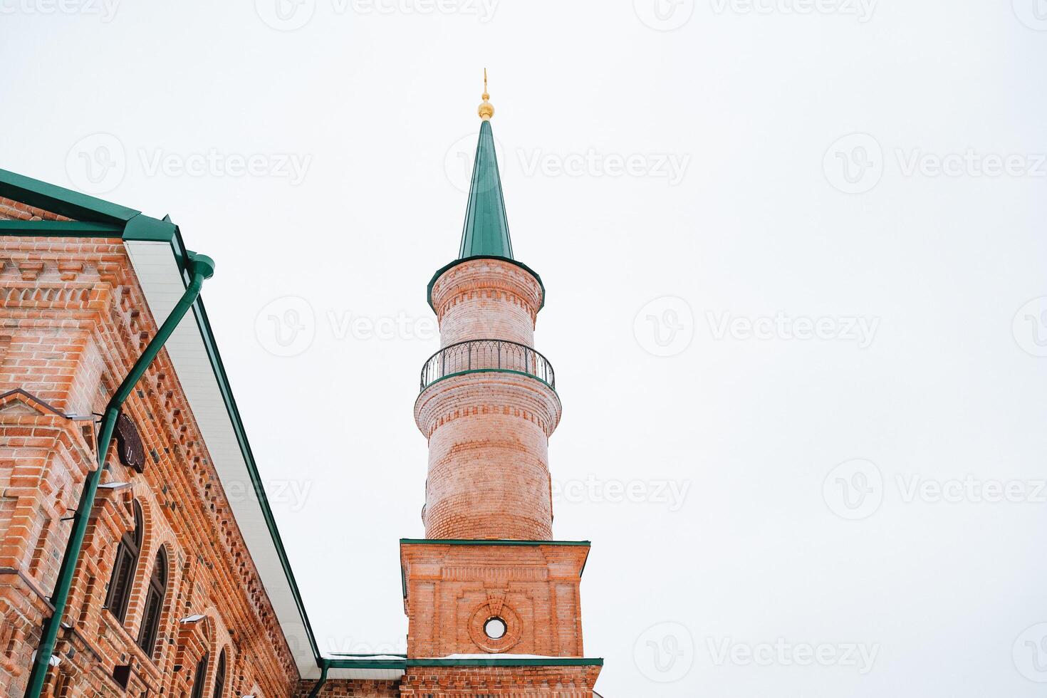 There is a brick building that features a green tower situated at the very top of its structure, creating a striking and memorable visual that stands out remarkably in the surrounding area photo
