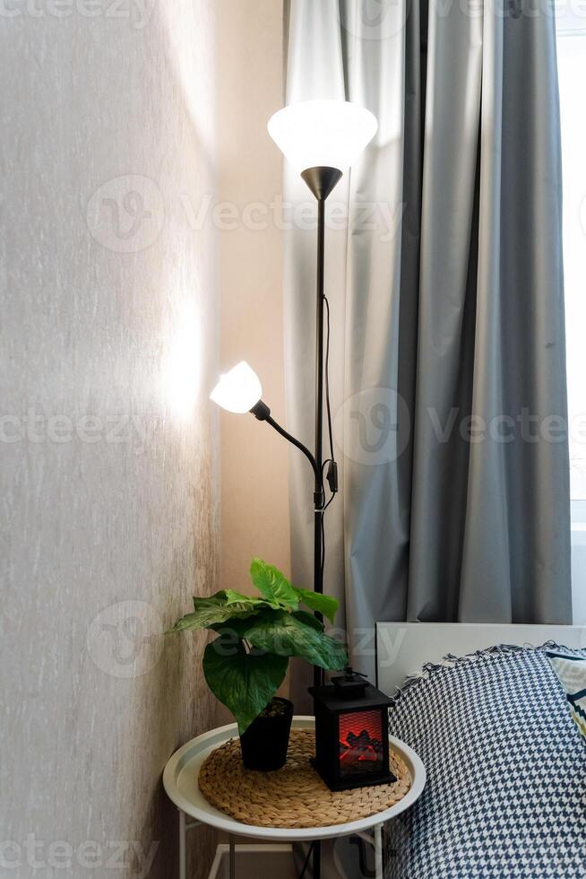 An elegantly designed lamp stands gracefully on a charming table that is situated next to a cozy bed, effectively creating a warm and inviting atmosphere that fills the entire room photo