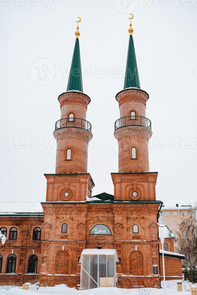 A charming brick building stands tall against the snowy backdrop, proudly showcasing two minaret towers that rise to the sky, becoming a stunning landmark in the winter landscape photo