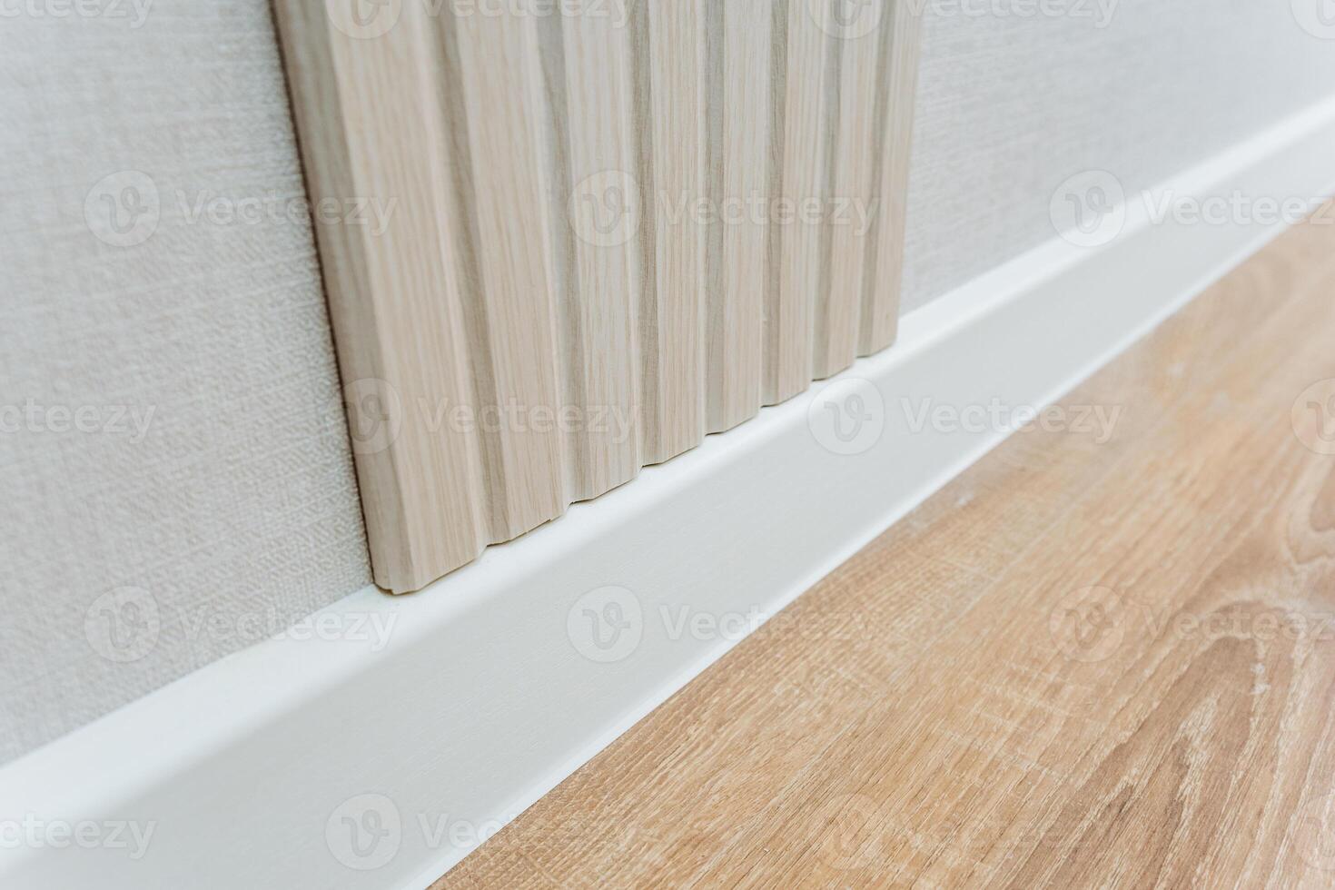 This image features a detailed closeup view of a wall that is adorned with a clean, white trim, alongside a beautifully polished wooden floor that adds character and warmth to the space photo