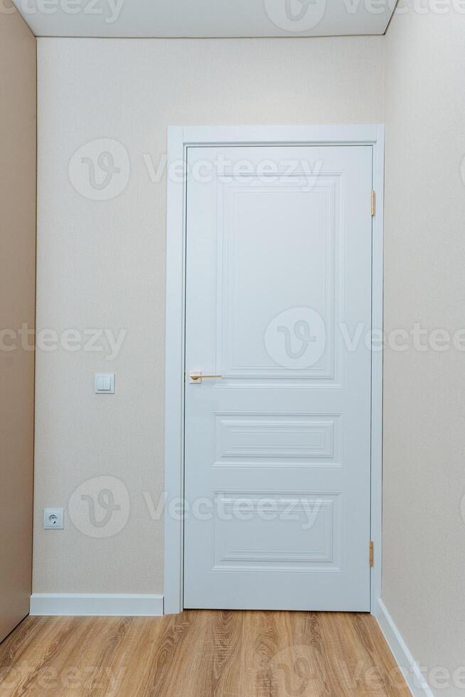 The scene depicts an empty room that features a pristine white door along with a beautifully polished wooden floor, creating a serene and inviting atmosphere in the space photo