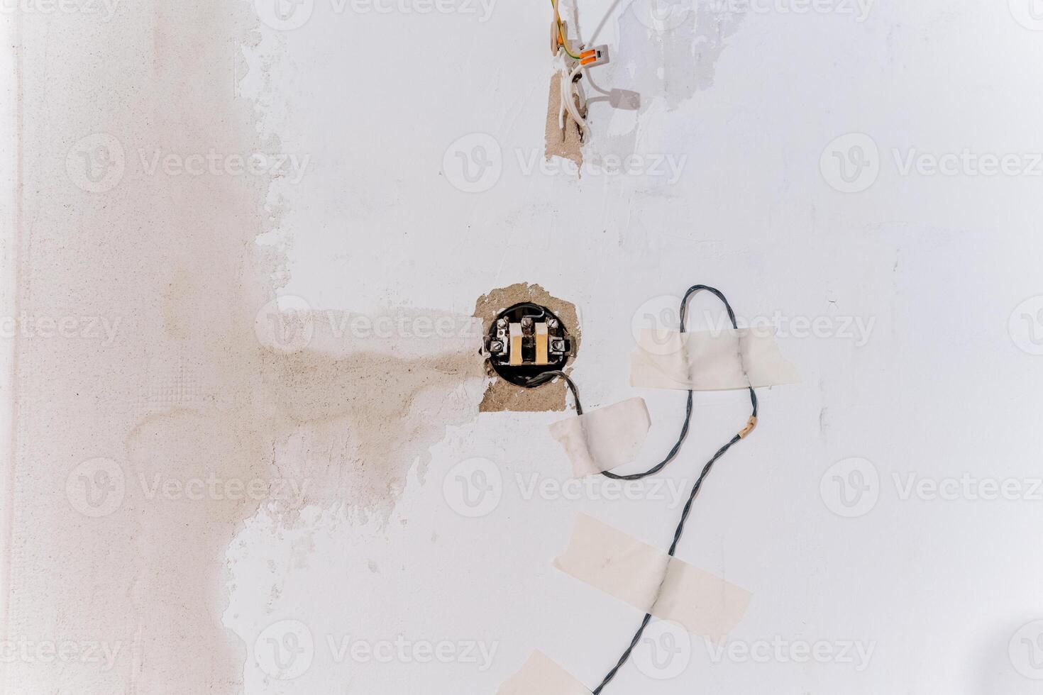 There is a white wall that features a significant hole in it, from which a wire is protruding, suggesting possible electrical work or modifications might have taken place photo