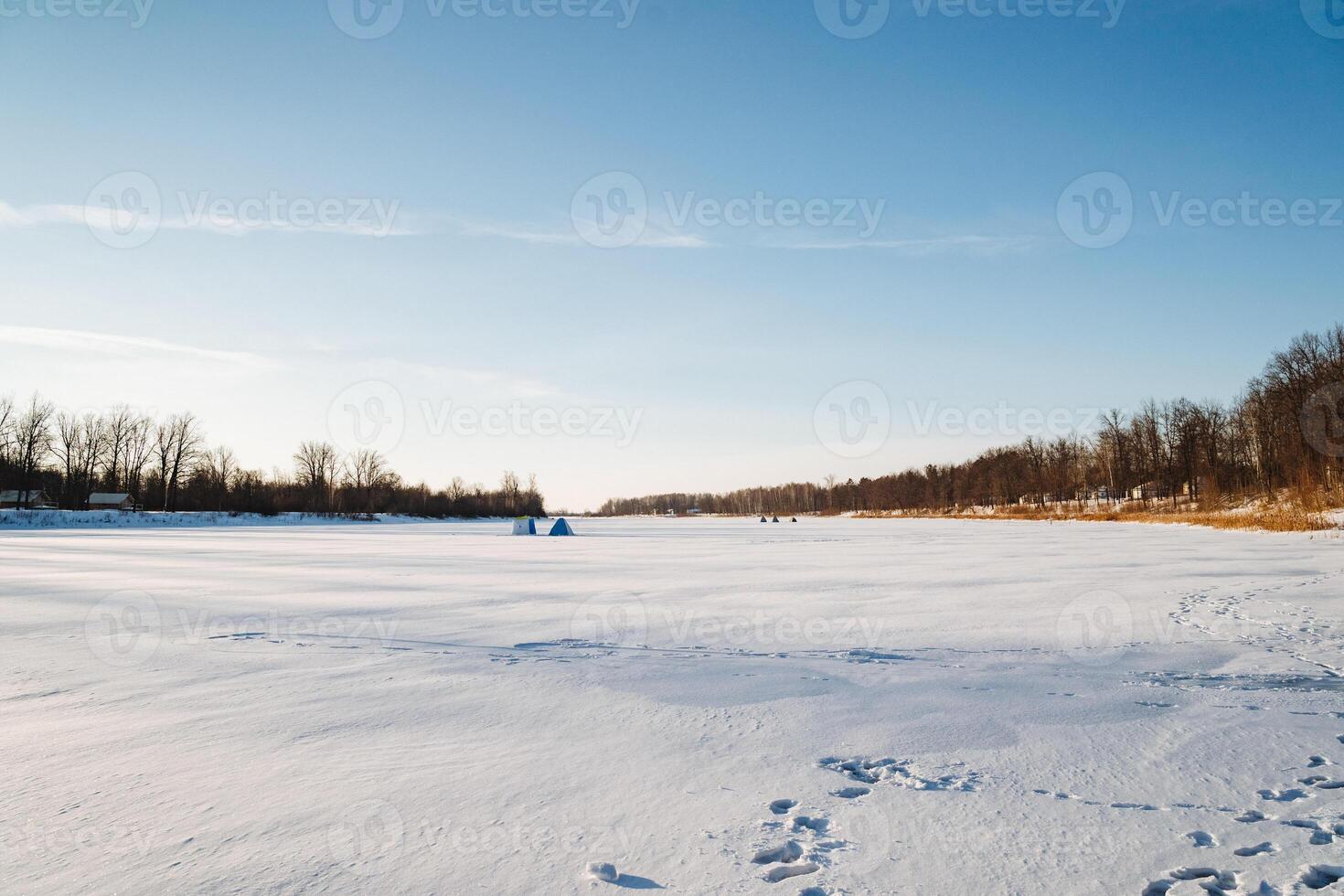 In a picturesque snowy field, there are distinct footprints imprinted in the abundant snow, while trees stand majestically in the background, creating a serene winter landscape photo