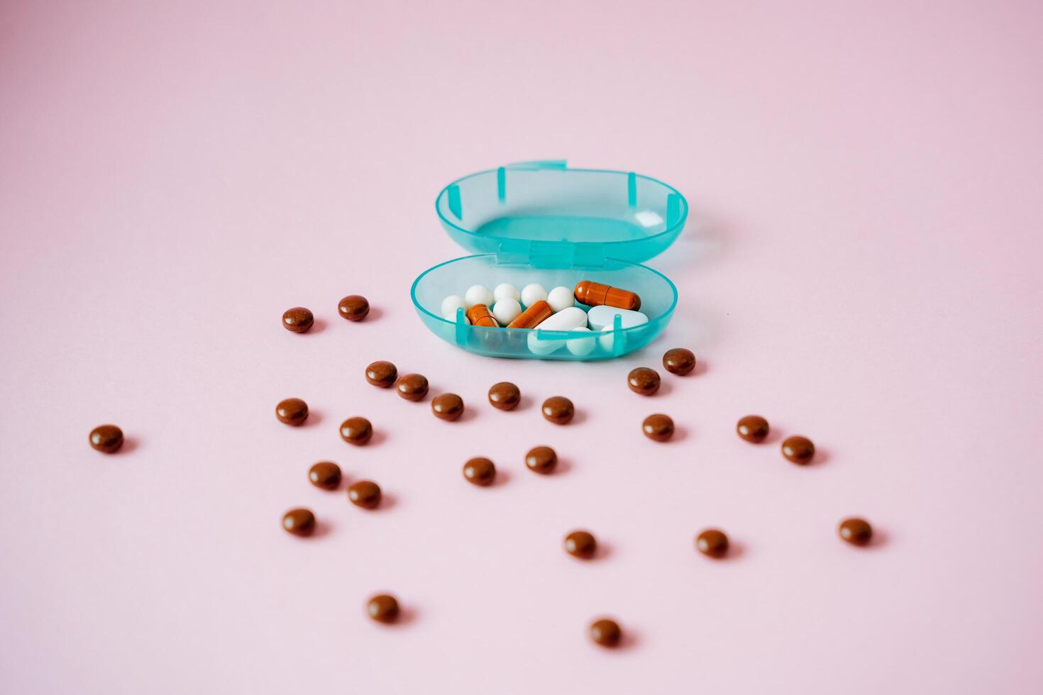 On a vibrant pink surface, there lies a blue container that is packed with an assortment of pills and brown balls, creating an intriguing display of various substances altogether photo