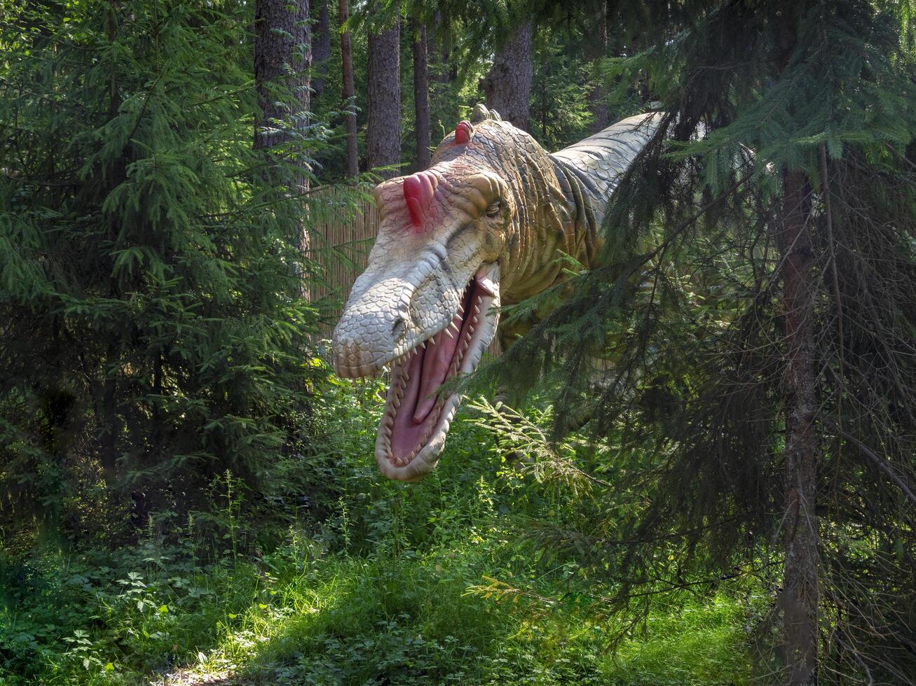 Saint-Petersburg, Russia - April, 05, 2024 Predatory dinosaur suddenly appeared from the dark thicket of the forest. Animation sculpture dinosaur. photo