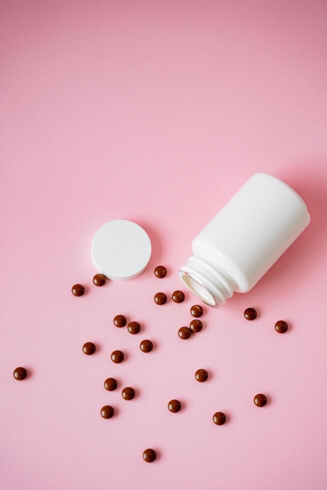 A large white bottle, packed with an array of colorful pills, precariously leans against a vibrant pink background. This tilt creates a striking, attentiongrabbing cascade of pills photo