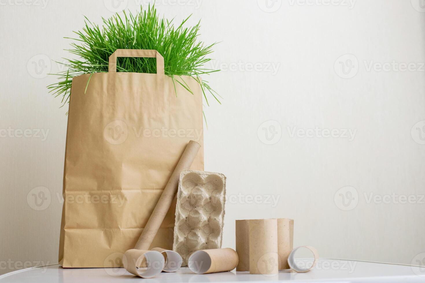 A paper bag with green grass stands on a white table. Household waste rollers made of cardboard photo