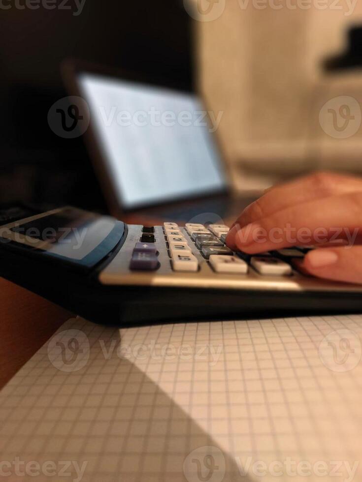 Close-up of female hand using calculator with laptop in office setting photo