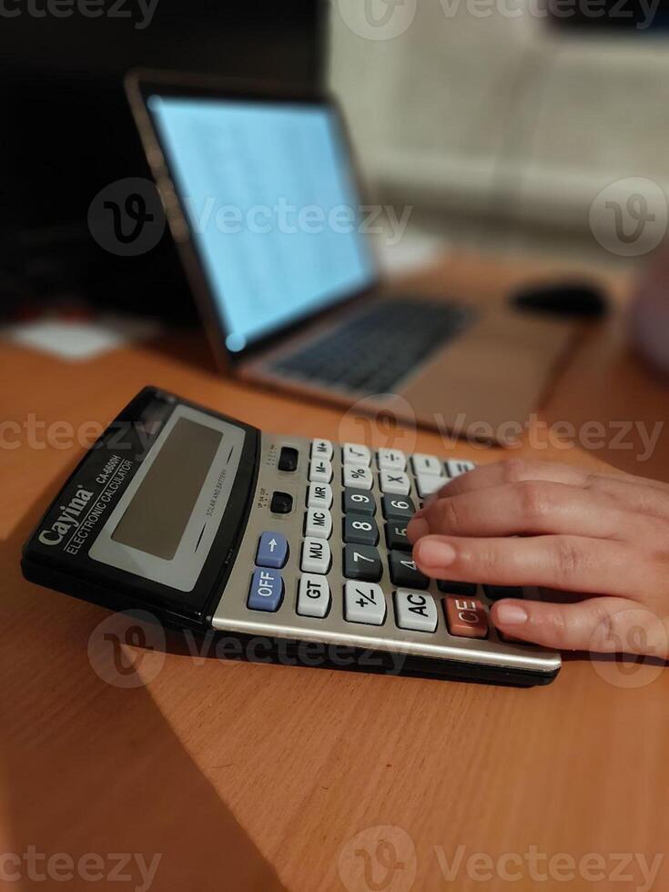 Hand using calculator at desk with laptop in background photo