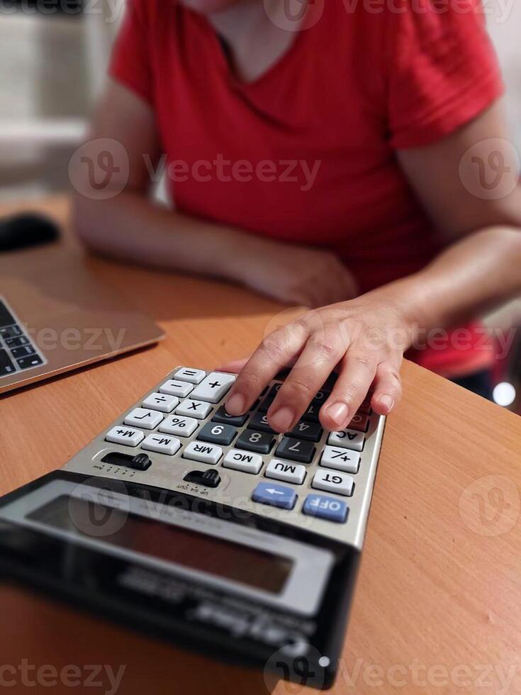 Caucasian young female using calculator at desk with laptop photo