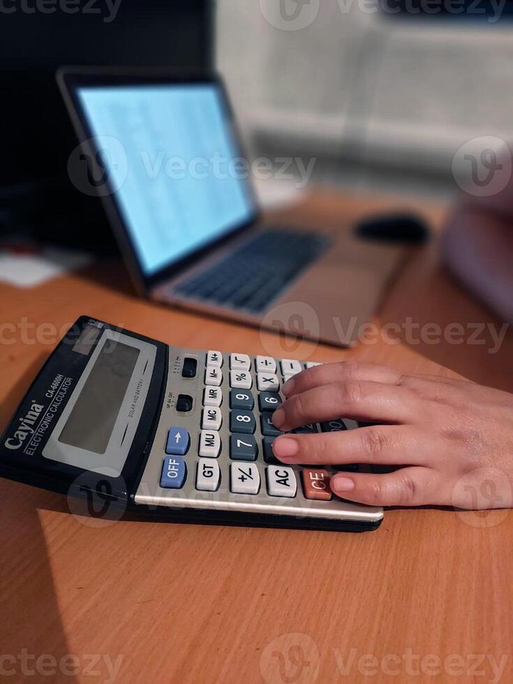 Adult using calculator and laptop for financial calculations at desk photo