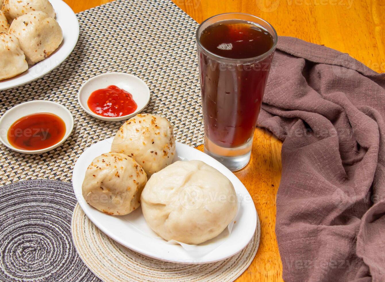 2 pan fried buns and 1 pepper pork bun with Dipping Sauces and a tall glass of iced tea isolated on napkin side view of taiwan dim sum food photo