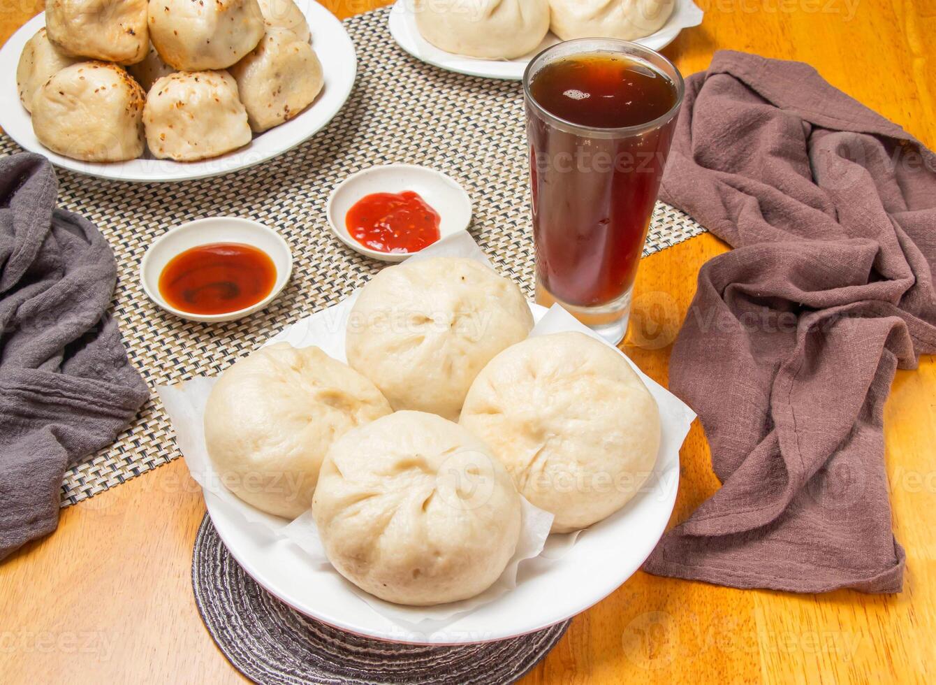 4 steamed pepper meat buns with Dipping Sauces and a tall glass of iced tea isolated on napkin side view of taiwan dim sum food photo