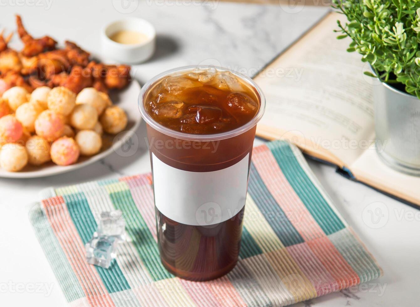 Iced Black tea served in plastic glass with ice cube isolated on napkin side view of taiwan cold drink photo