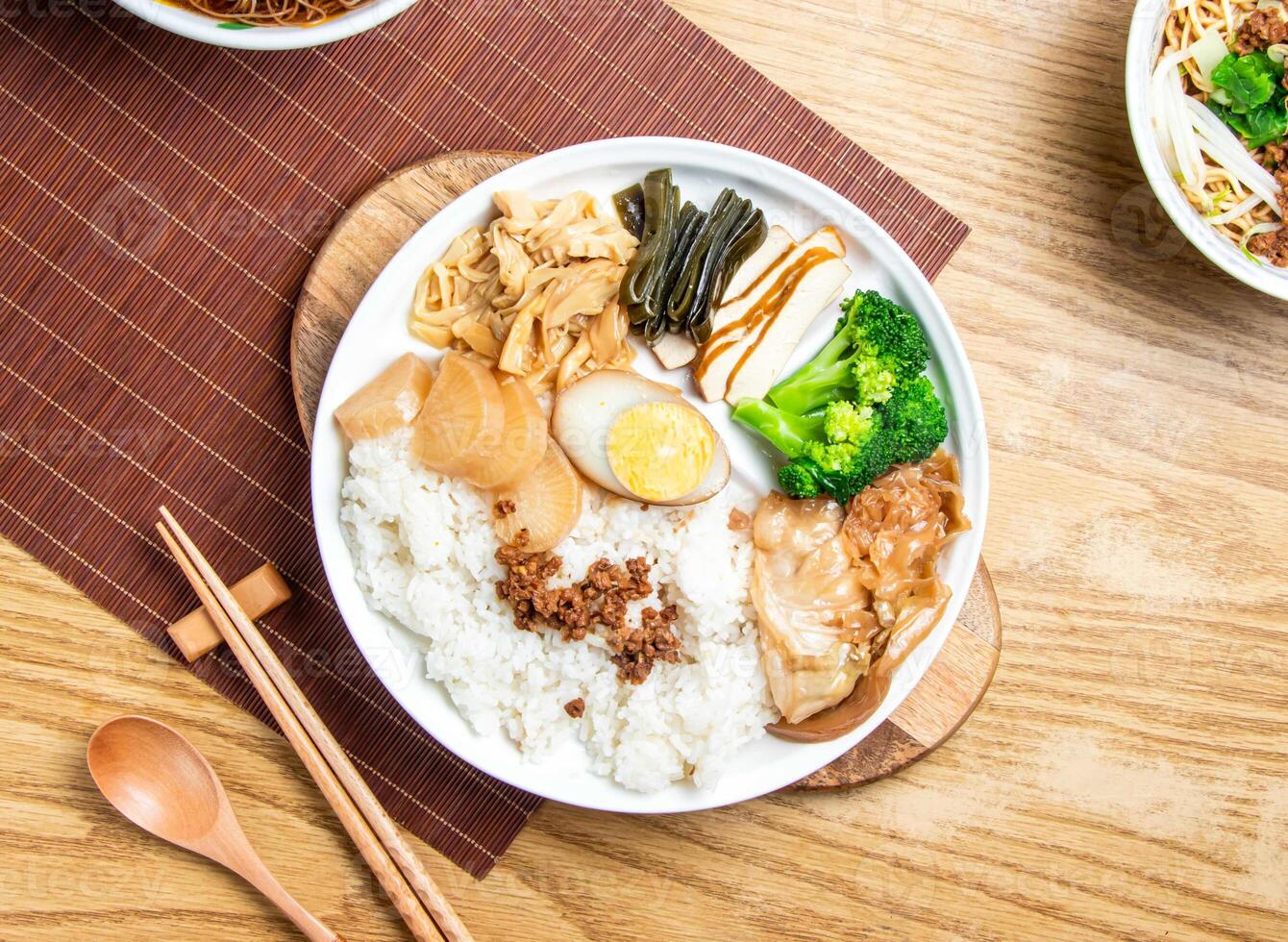 taiwanese lu rou fan include rice, broccoli, boiled egg, tofu, minced pork, braised pork belly, and cabbage served in plate with chopsticks and spoon isolated on wooden board top view of taiwan food photo
