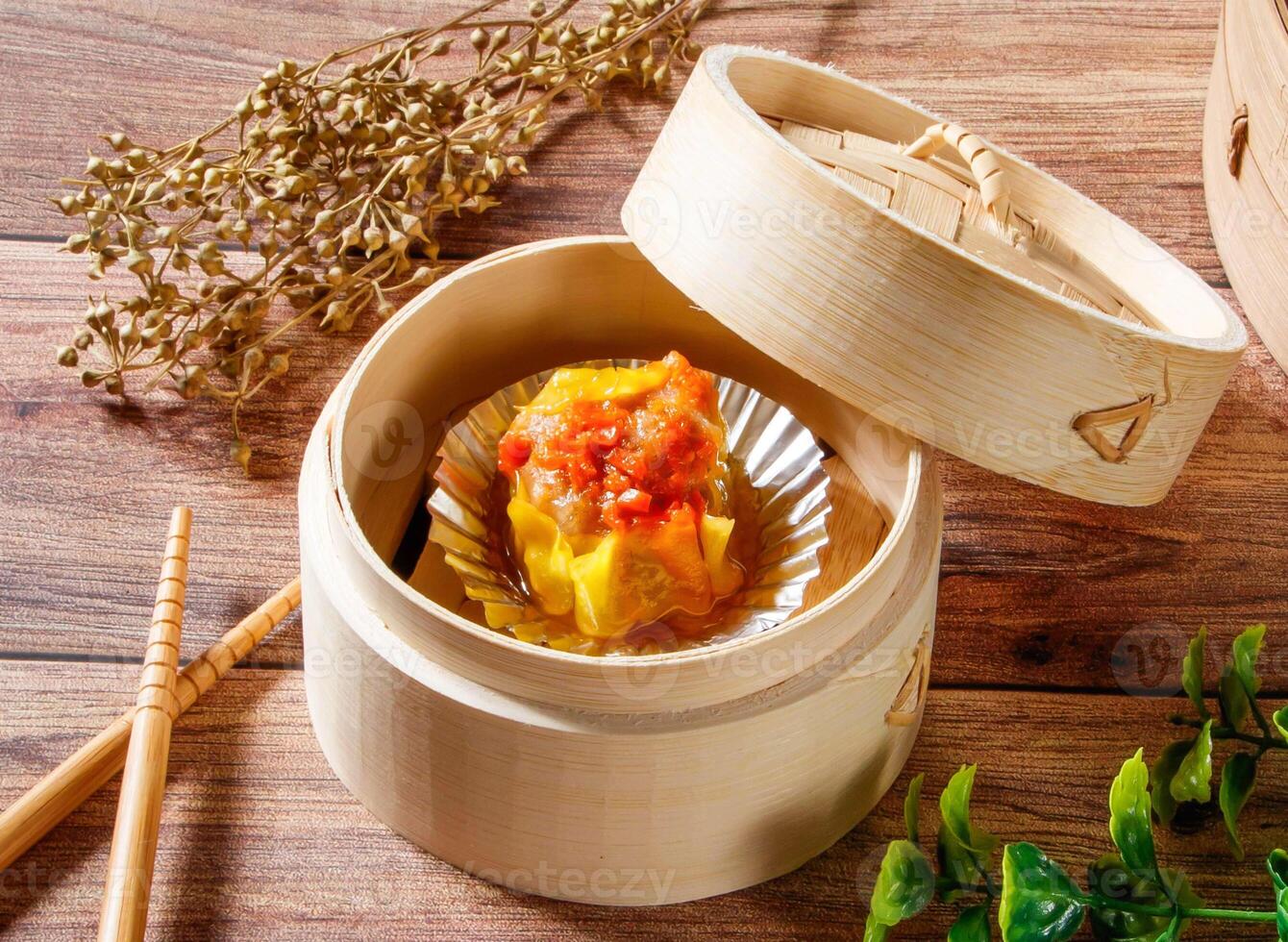 Crab Roe Siu Mai Steamed Dumpling in Bamboo Steamer with chopsticks isolated on wooden table side view of dim sum taiwan food photo