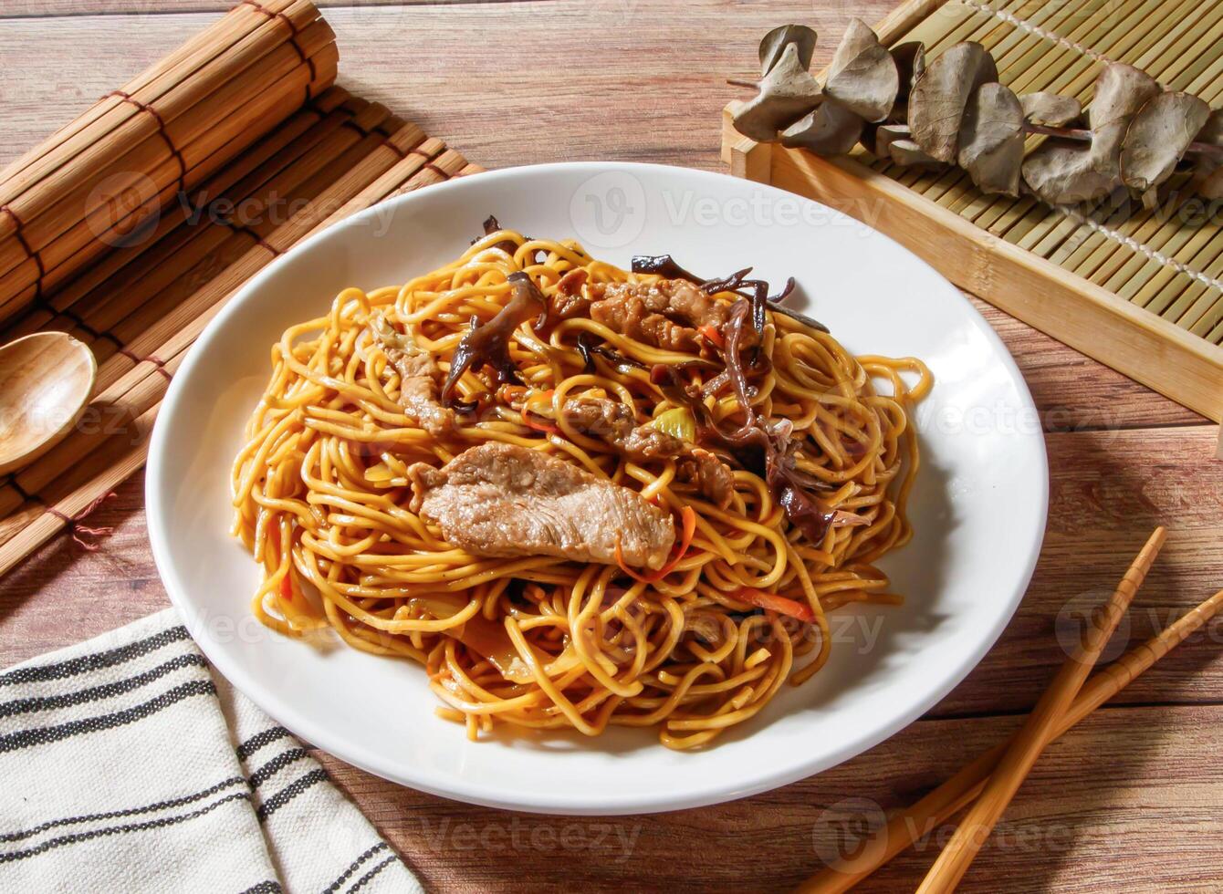 Mu Shu Stir Fried Noodles with Shredded Pork and Vegetables served in plate with chopsticks and spoon isolated on wooden table side view of taiwan food photo