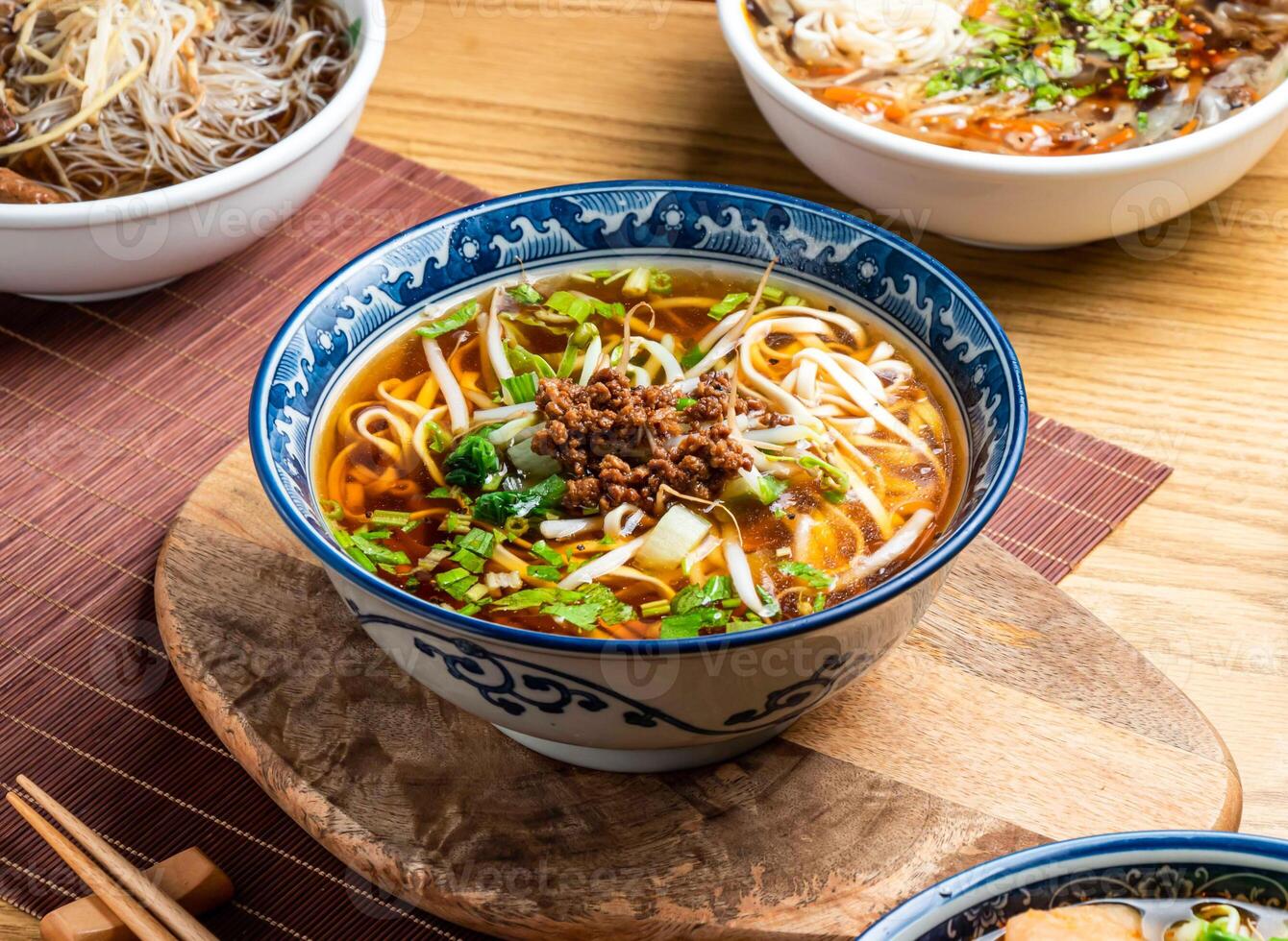 Taiwanese Noodle Soup topping with mince meat served in bowl with chopsticks and spoon isolated on wooden board side view of taiwan food photo