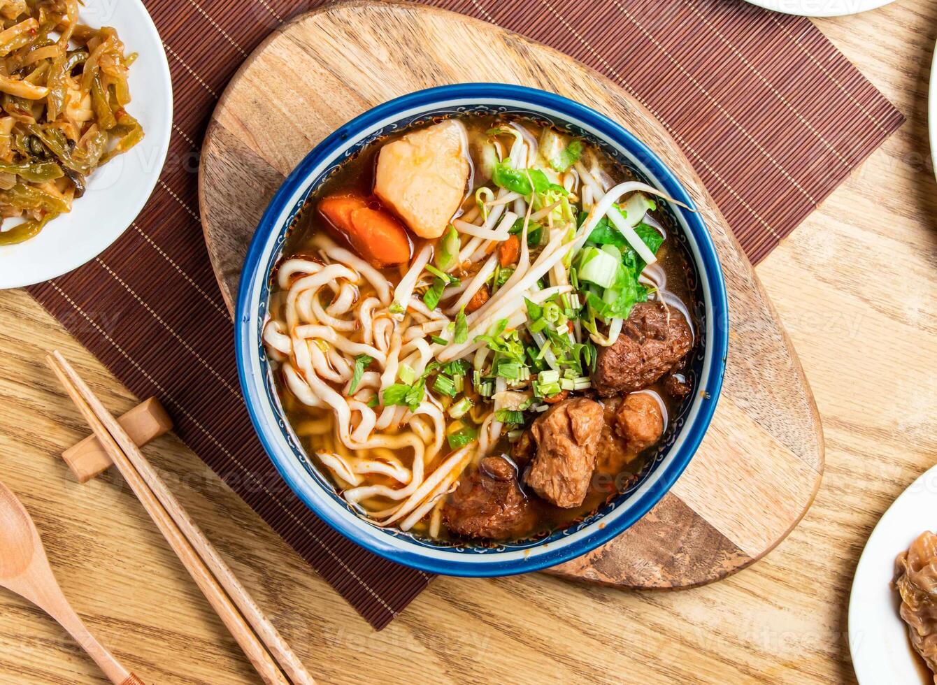 Vegetarian Beef Noodle Soup topped with green onion and coriander served in bowl with chopsticks and spoon isolated on wooden board top view of taiwan food photo