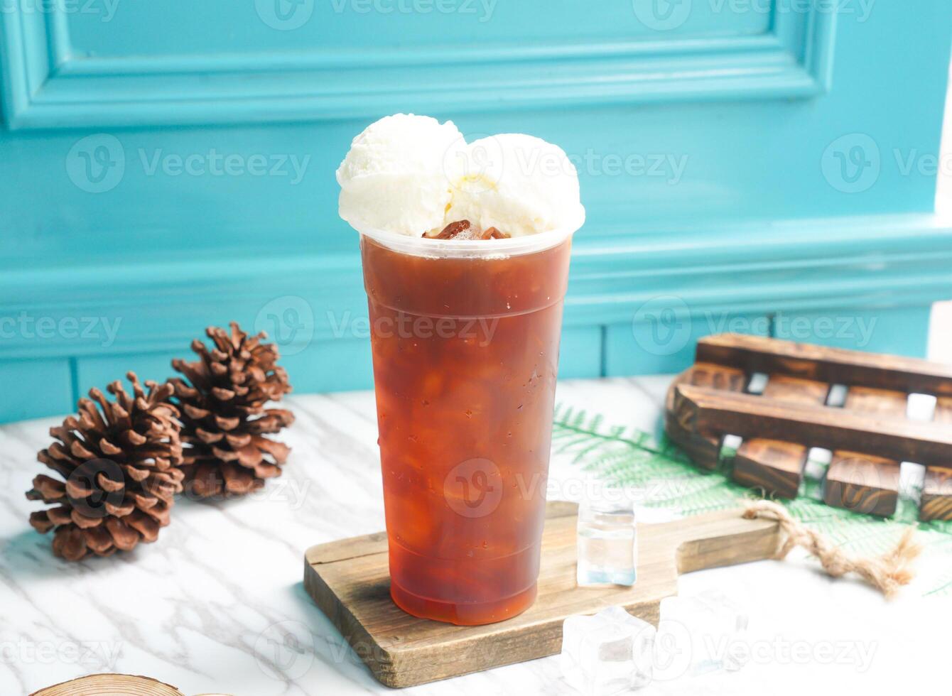 iced Black tea with two scoop of vanilla ice cream and ice cube in tall glass served on a wooden board side view of taiwan cold drink photo