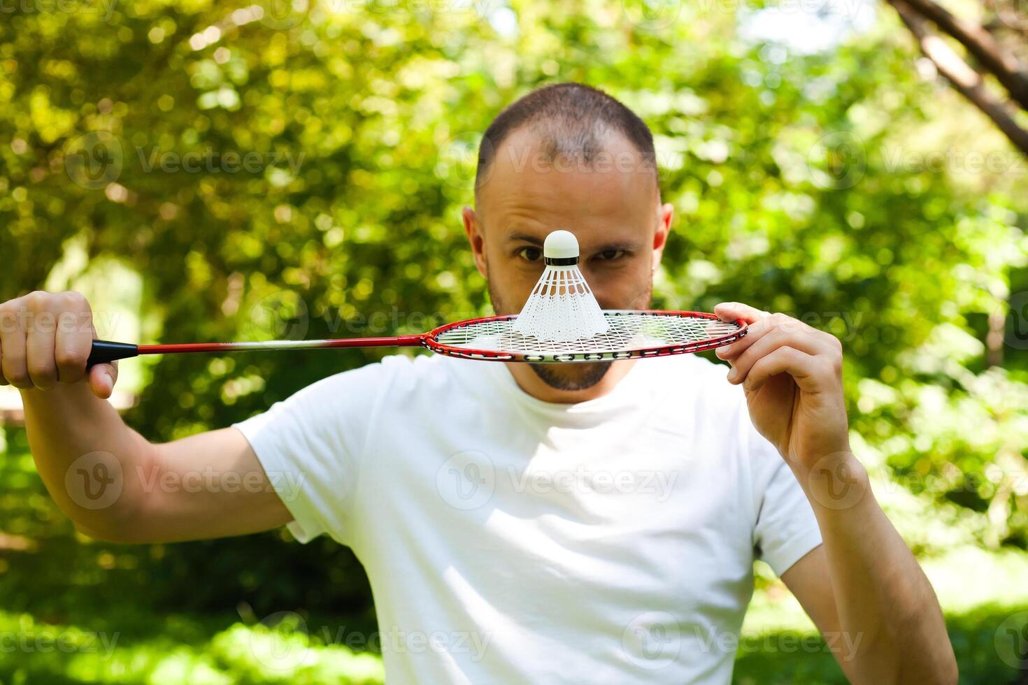 Young man winks and covers her face with a racket badminton. Lifestyle, vacation, sport and fun. Close-up. photo