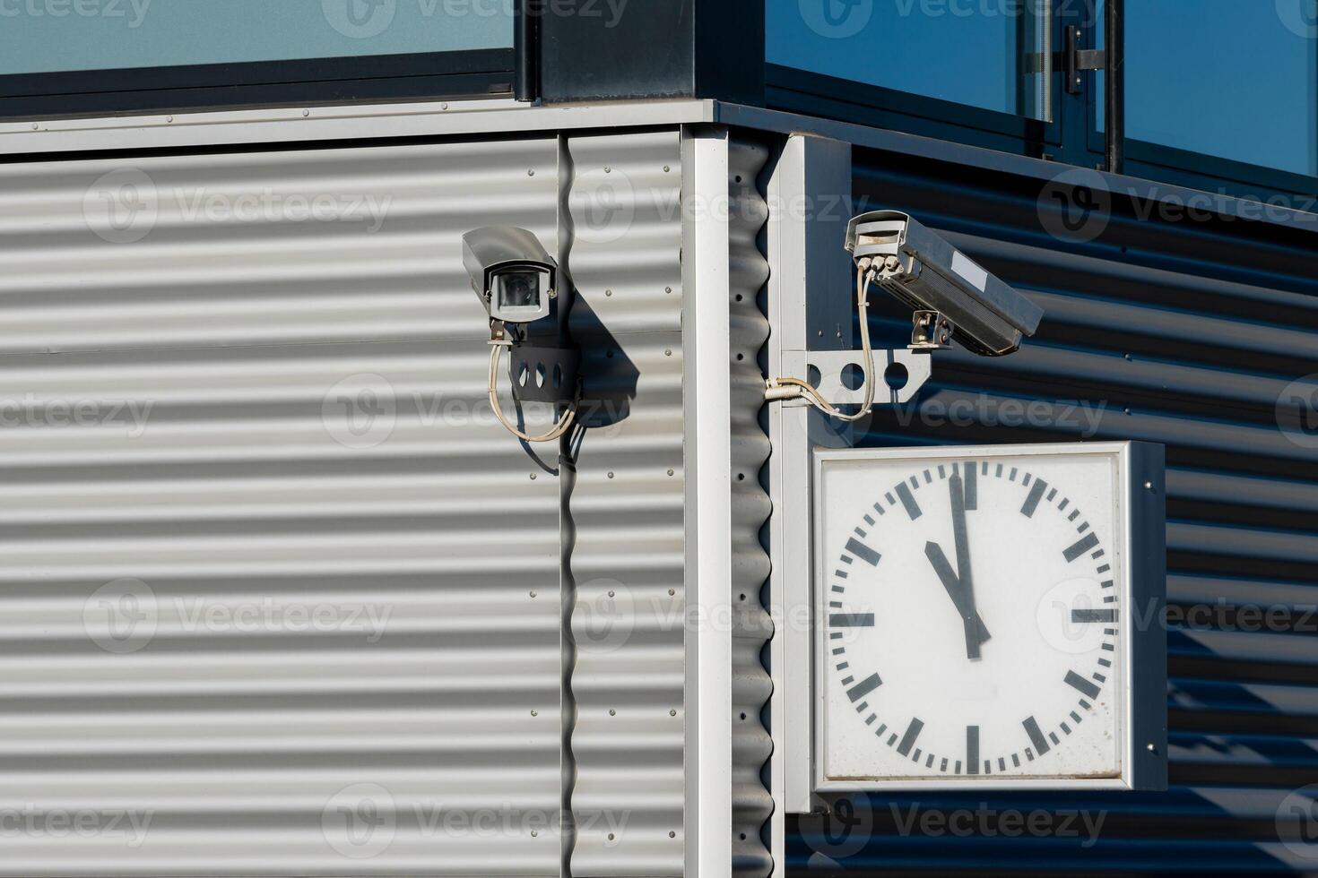 Security cameras and clock mounted on modern building exterior photo