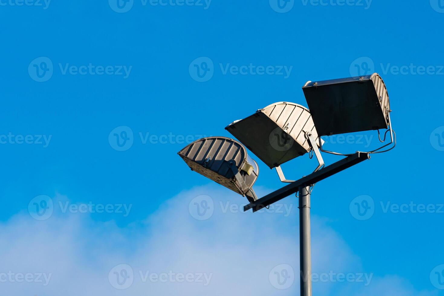 Three evenly spaced light fixtures are mounted on a tall pole against photo