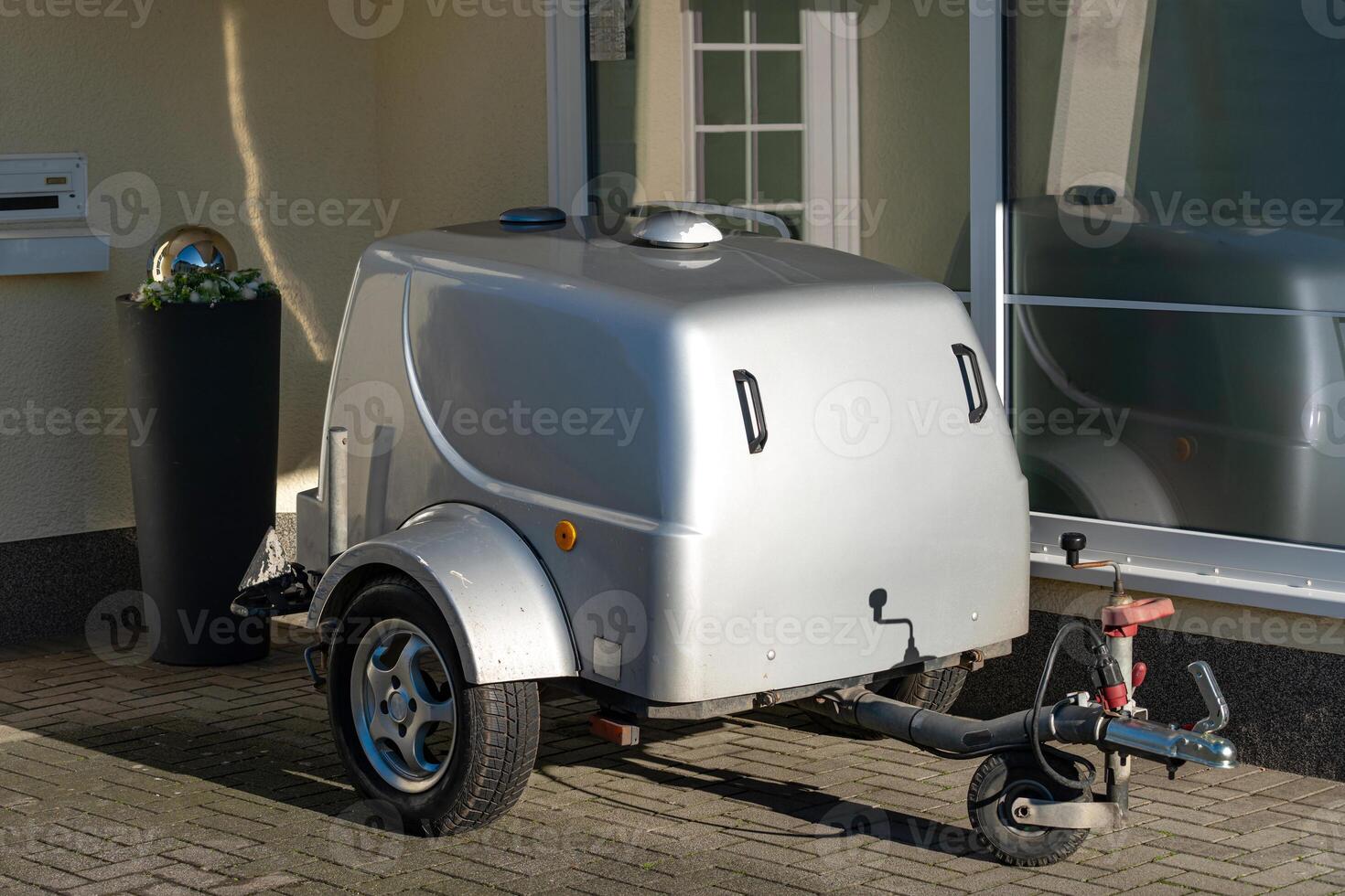 Compact silver trailer parked outside a building during daylight photo