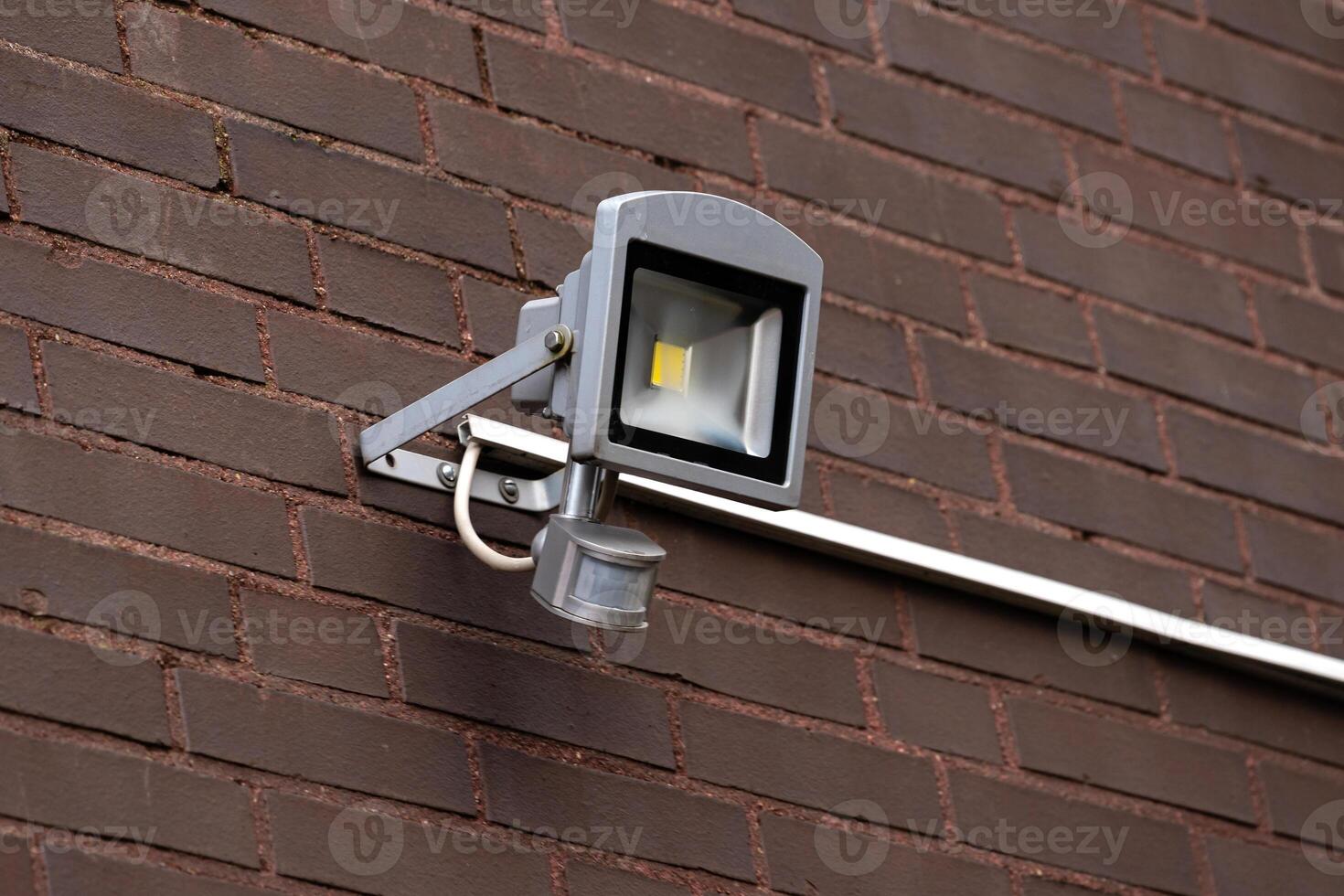 Outdoor motion sensor light mounted on a brick wall near entrance photo