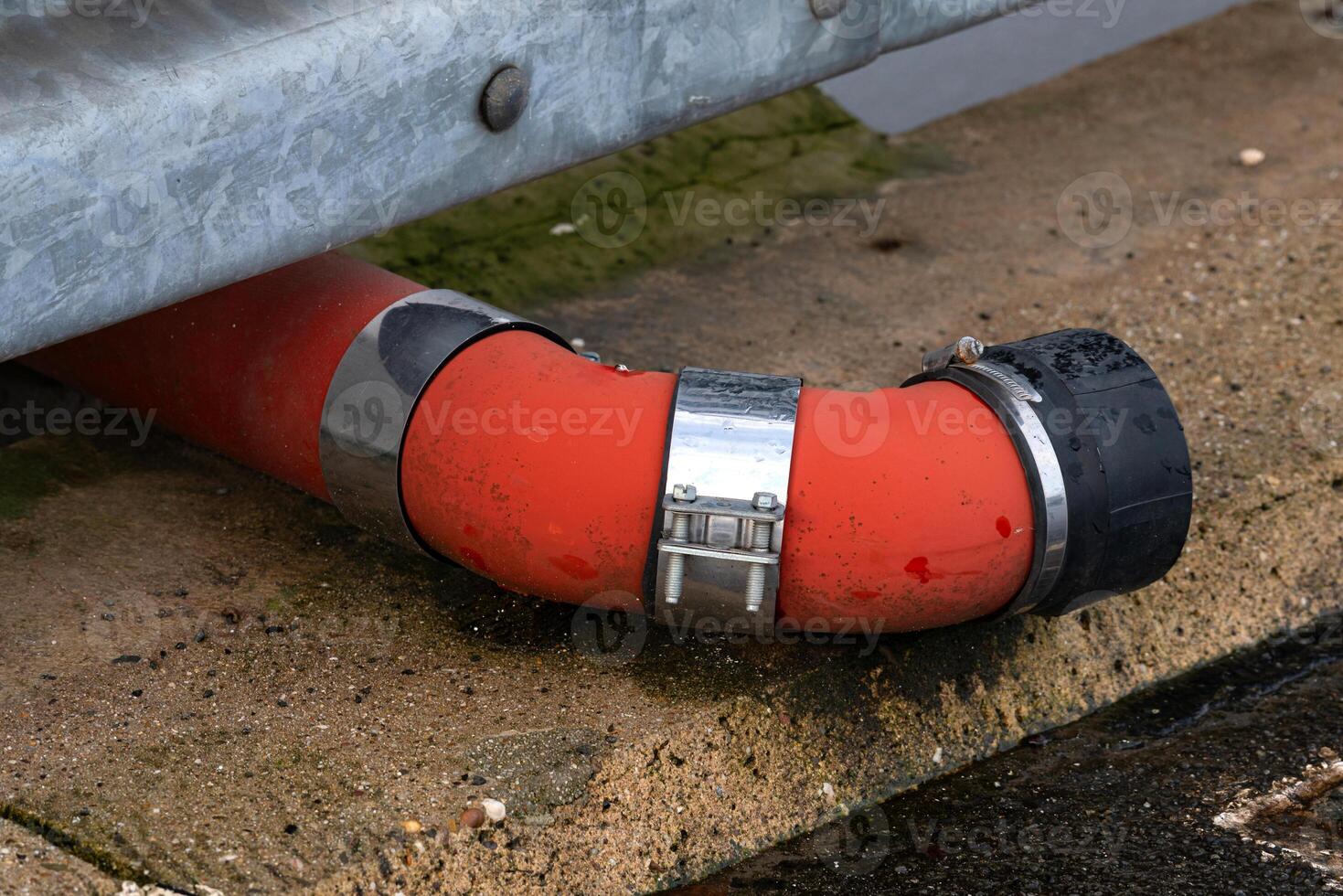 Red drainage pipe connecting to concrete surface in industrial area photo