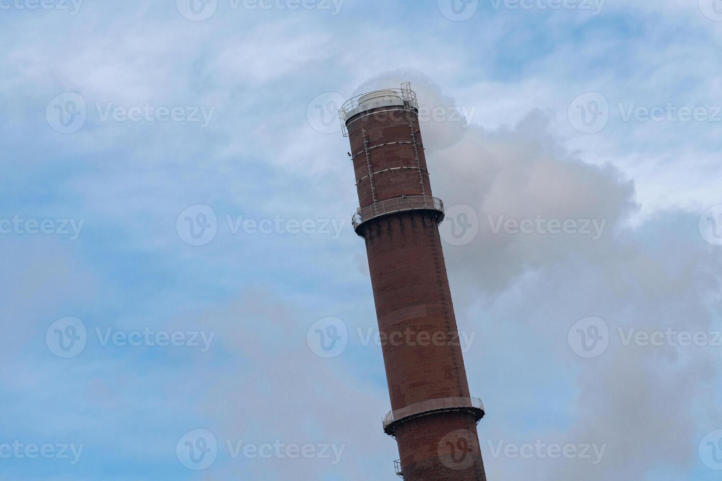 Smoke rising from an industrial chimney in a clear blue sky photo