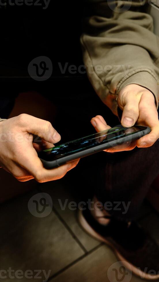 young man playing mobile game with rapid finger movements, hands illuminated by warm soft lighting, captured from a top-down view, showcasing an intense and focused gaming moment in a cozy atmosphere photo
